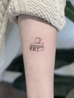 a woman's arm with a stack of books and a cup tattoo on it