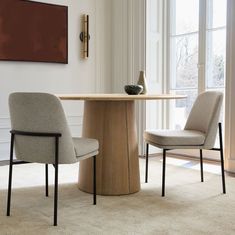 two chairs sitting at a round table in front of a window with a painting on the wall