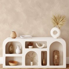 a white shelf with vases and other items on it in front of a beige wall