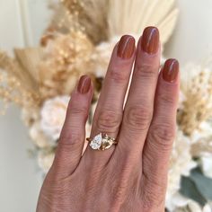 a woman's hand with a ring on it and flowers in the back ground