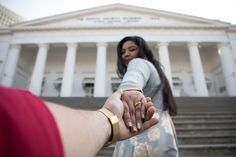 a woman holding the hand of a man in front of a white building with columns