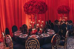 a room filled with lots of tables covered in black cloths and red floral centerpieces