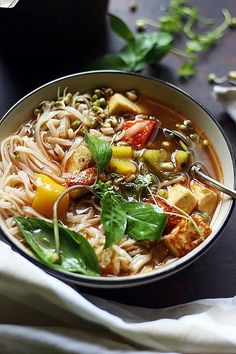 a bowl of soup with noodles, vegetables and tofu on the side next to a napkin