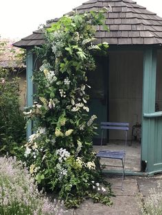 a small garden shed with a bench and flowers growing on the outside wall next to it