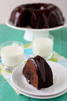 a chocolate bunt cake on a white plate next to two glasses of milk and a glass of milk