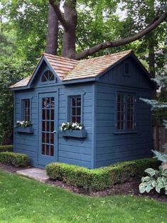 a small blue shed in the middle of a yard with trees and bushes around it