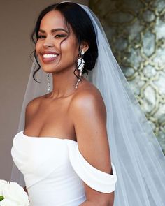 a woman wearing a wedding dress and holding a bouquet smiles at the camera while standing in front of a wall