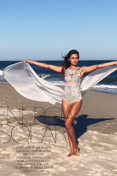 a woman is posing on the beach with her arms outstretched