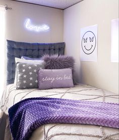 a bed with purple and white pillows in a bedroom next to a window that reads love you stay in bed