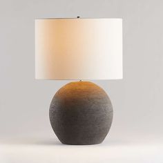 a gray table lamp with a white shade on the base and a light in front of it