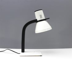 a black and white desk lamp on top of a white table next to a gray wall