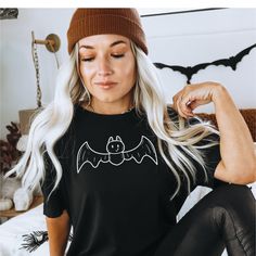 -DESCRIPTION- Introducing our charming Cute Bat Fall T-Shirt for Women, the perfect addition to your autumn wardrobe that combines adorableness and Halloween spirit! 🦇🍂 This delightful t-shirt features a cute cartoon bat, adding a touch of whimsy to your fall attire. The design perfectly captures the essence of the season, making it an ideal choice for Halloween enthusiasts and those who simply adore autumn. Crafted from soft, high-quality fabric, this tee is incredibly comfortable and will keep you cozy as the weather turns cooler. Whether you're sipping pumpkin spice lattes, picking apples, or getting into the Halloween spirit, this shirt is a versatile and stylish choice. Looking for a thoughtful gift for her? The Cute Bat Fall T-Shirt is the perfect option. It's a versatile piece tha Spooky Black T-shirt For Fall, Black Spooky Crew Neck Top, Casual Black Halloween Top, Black Crew Neck Top For Halloween, Black Short Sleeve Top For Halloween, Trendy Halloween Short Sleeve T-shirt, Trendy Halloween Crew Neck T-shirt, Halloween Trendy Crew Neck Top, Spooky Black Pre-shrunk Tops