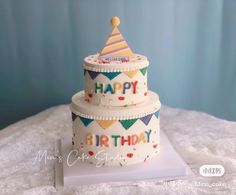 a three tiered birthday cake sitting on top of a white tablecloth covered table