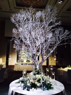 a white table topped with a tree covered in lights and flowers next to a chandelier