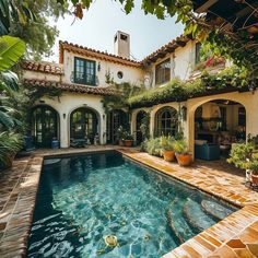 an outdoor swimming pool surrounded by greenery and potted plants in front of a house