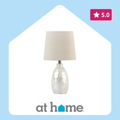 a table lamp with a white shade on it and the words at home above it