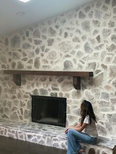 a woman sitting in front of a stone fireplace