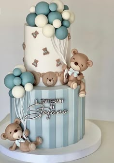 a three tiered blue and white cake with teddy bears on the top, balloons in the air