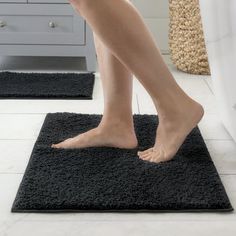 a woman standing on top of a black rug in front of a white dresser and mirror