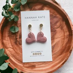 the pink heart earrings are sitting on top of a wooden plate next to a plant