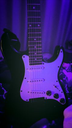 an electric guitar sitting on top of a table in front of a purple light and curtains