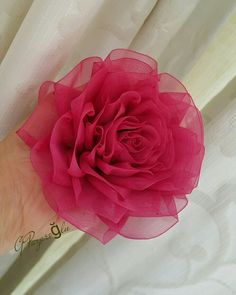 a person's hand holding a pink flower on top of a white cloth curtain