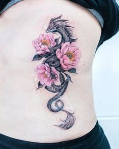 a woman's stomach with pink flowers and a dragon tattoo on her side ribcage