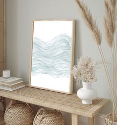 a white vase sitting on top of a wooden table next to a framed art print