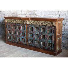 an old wooden sideboard with many different colors and designs on the doors, in front of a stone wall