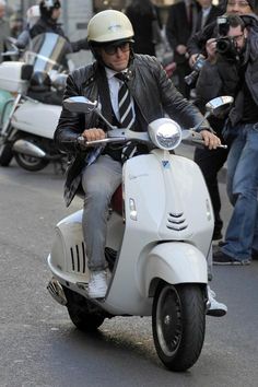 a man riding on the back of a white scooter down a city street