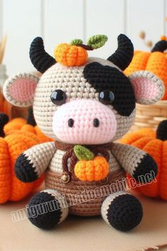 a small crocheted cow sitting on top of a table next to pumpkins