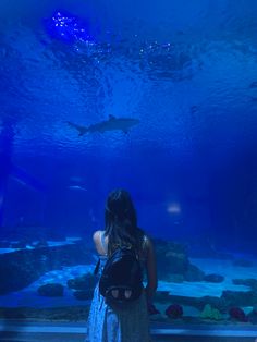 a woman standing in front of an aquarium tank looking at sharks and other marine life