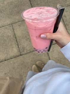 a person holding a pink drink in their left hand and looking down at the ground