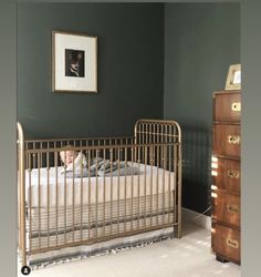 a baby in a crib next to a dresser with a framed photograph on the wall