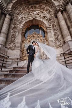 a bride and groom standing in front of an ornate doorway with their veil blowing in the wind