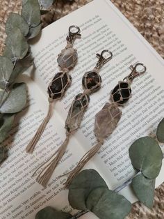 five pieces of jewelry sitting on top of an open book next to eucalyptus leaves and ivy