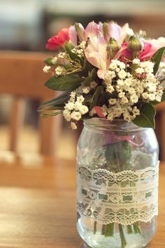 a glass jar with flowers in it sitting on a wooden table next to a chair