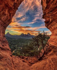 the sun is setting over mountains and trees from inside a rock formation with a tree in the foreground