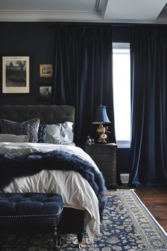 a bedroom with dark blue walls and white bedding, black drapes, an upholstered headboard