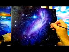 a person is holding a paintbrush in front of a painting with stars and planets on it