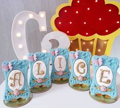 a table topped with cookies covered in frosting next to a cupcake shaped cake