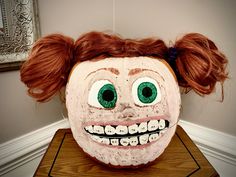 a creepy mask with green eyes and red hair on top of a wooden table in front of a white wall