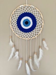 a crocheted dream catcher with an evil eye on the front and white feathers around it