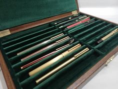 an open wooden box containing several different types of pens and pencils in velvet cases