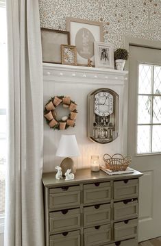 a clock on the wall above a dresser in a room with white walls and curtains