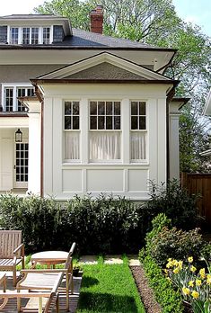 a house with lawn chairs in front of it and flowers around the back yard area