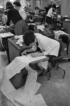 an office filled with people sitting at desks and working on paper work sheets in front of them