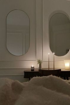 two round mirrors are on the wall above a table with candles and a fur rug