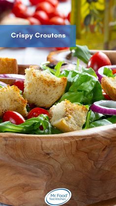 a wooden bowl filled with salad and croutons on top of a table next to tomatoes