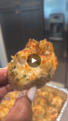 a hand holding up a piece of food in front of a pan filled with macaroni and cheese